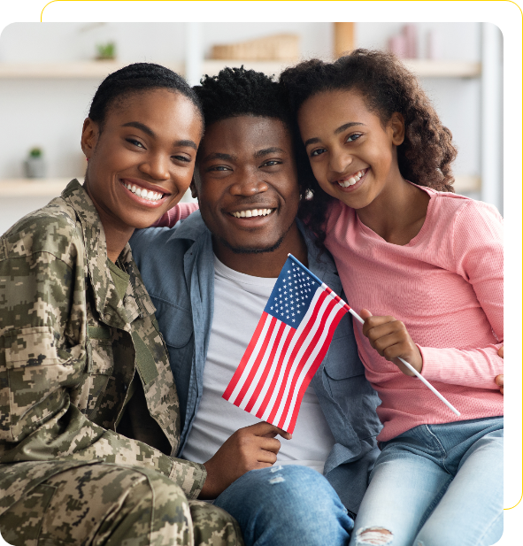 Three people sitting together, smiling. The person on the left is wearing a military uniform. The person in the middle is holding a small American flag. They are in a cozy indoor setting.