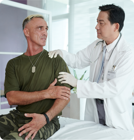 Doctor examines a seated man in military attire, placing a hand on his shoulder.